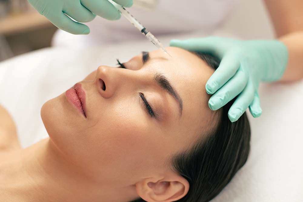 A woman lying down and receiving an injectable in her forehead